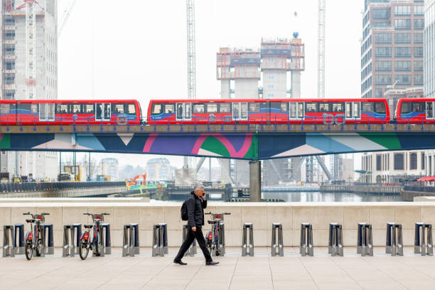 a businessman walking on reuters plaza in canary wharf with dlr trains passing and building site of newfoundland in the background - docklands light railway imagens e fotografias de stock