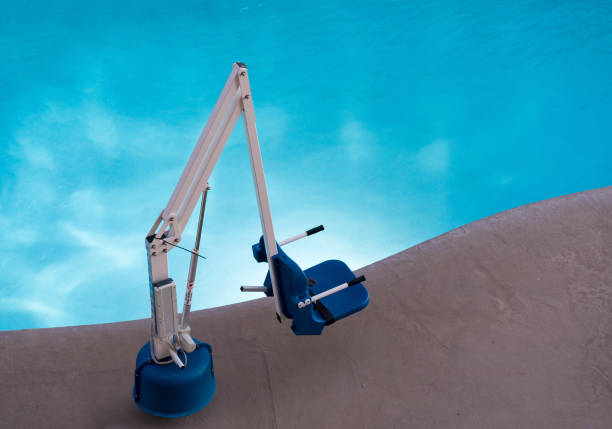 Disabled person poolside lift by swimming pool Disabled person pool lift or hoist meets ADA standards installed by swimming pool to lower people into water outdoor elevator stock pictures, royalty-free photos & images