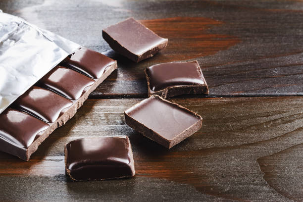 istock Bitter, dark chocolate bar in foil and broken cubes on wooden background 696413664
