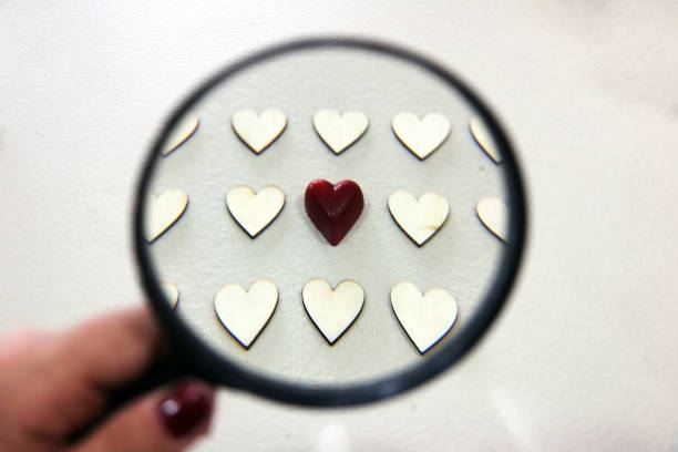 red chocolate heart among wooden hearts seen through the lens - magnifying glass lens holding europe imagens e fotografias de stock