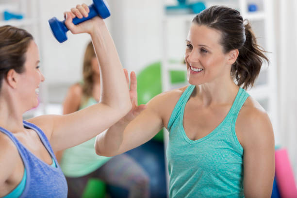 istock Physical Trainer encourages client to raise barbell high 696450088