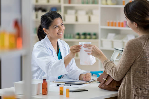 smiling female pharmacist hands medication to customer - prescription doctor rx pharmacist imagens e fotografias de stock