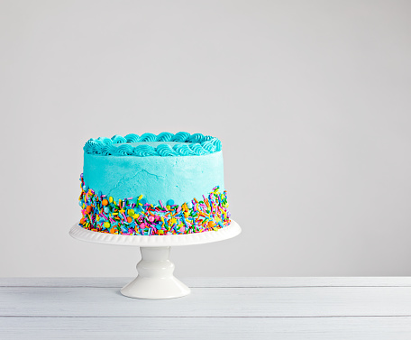 Blue buttercream cake with colorful sprinkles over a light grey background.
