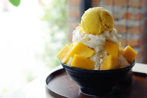 Mango shaved ice, also known as Mango Bingsu Korean dessert, served with sticky rice, whipped cream and mango ice cream on the table, Smoke of dry ice.