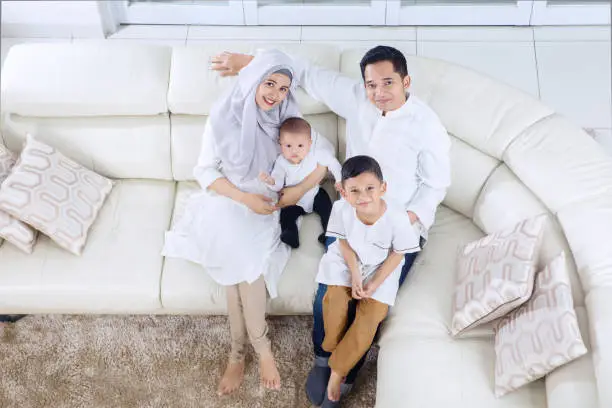 Top view of muslim parents and children sitting on the sofa while smiling together at home