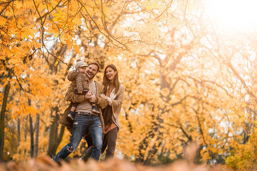 Young happy parents having fun with their small boy while running in the park during autumn day.