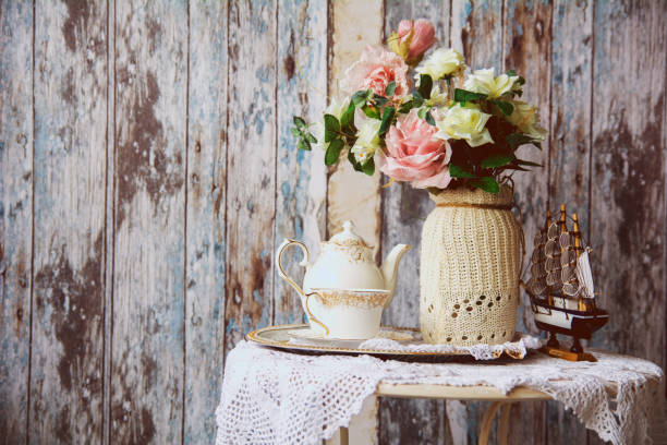 Porcelain teapot and cup on a table with a vase with artificial flowers on a background of the old wooden walls. Small boat on the table