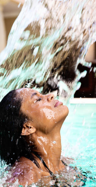istock Beautiful girl standing under spa pool's waterfall 696533034