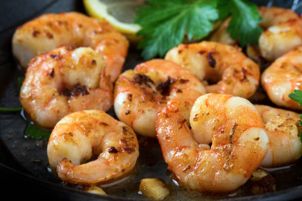 prawns shrimps roasted in a black pan with garlic, lemon and italian parsley garnish, close up prawns shrimps roasted in a black pan with garlic, lemon, spices and italian parsley garnish, close up, selected focus, narrow depth of field marinade stock pictures, royalty-free photos & images
