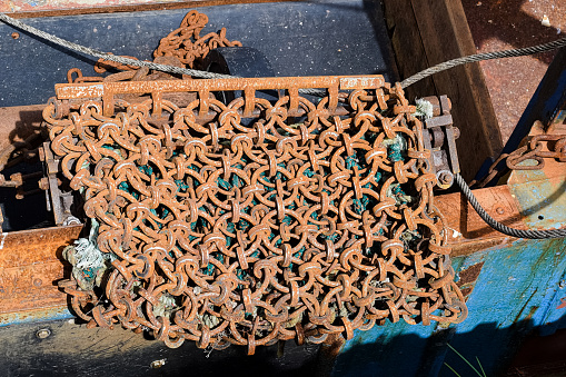 Close-up of rusty scallop dredger equipment lying on a blue knotted rope placed on the deck of a boat