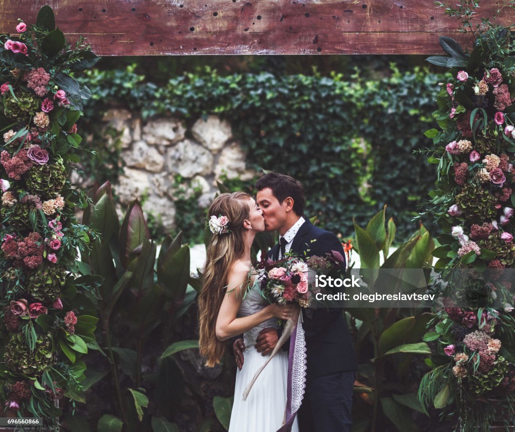 Incredibile cerimonia nuziale con molti fiori freschi in stile rustico. Sposi felici che si baciano - Foto stock royalty-free di Matrimonio