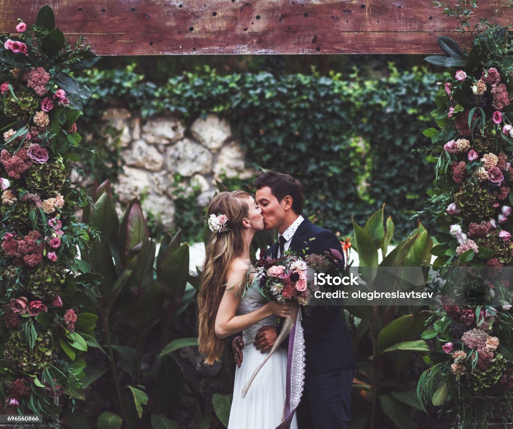 Amazing wedding ceremony with a lot of fresh flowers in Rustic style. Happy newlyweds kissing Wedding Stock Photo