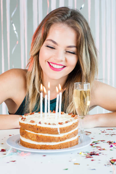 Pretty girl looking at lit candles on birthday cake for celebration stock photo