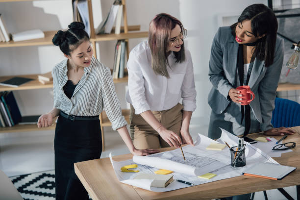 istock Smiling young businesswomen working with blueprints and discussing project in office 696569880