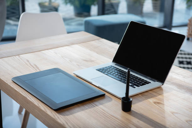 istock laptop with blank screen and graphics tablet on wooden tabletop at office 696573840