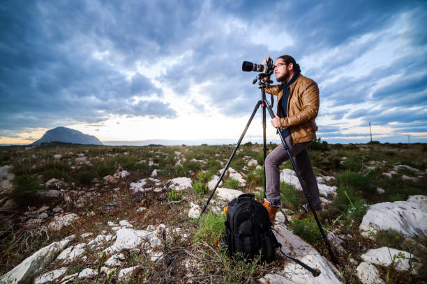 istock Young attractive photographer making photos with camera on tripod at sunset 696574212