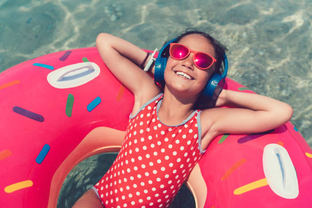 Little girl in life preserver enjoying the music Smiling girl floating on water and listening to the music girls laying on beach stock pictures, royalty-free photos & images