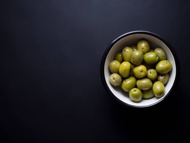 istock Green olives in bowl isolated on black 696585394