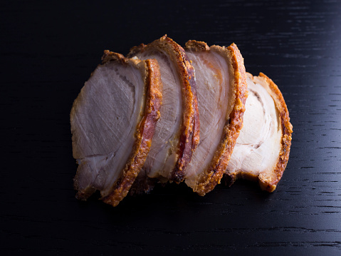 Slices of roasted pork with crispy crackling, isolated on black background