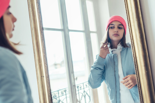 french stylish teenage girl with bore jacket and beanie  looking herself in  mirror