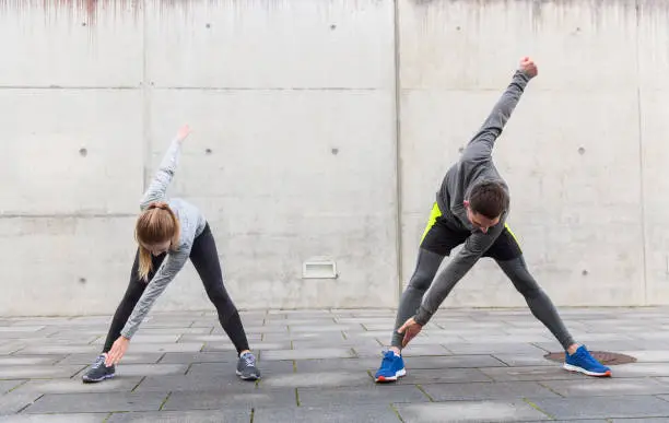 fitness, sport, exercising, training and people concept - close up of couple stretching on city street