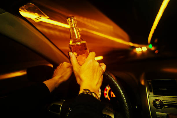 Car driver holds an alcholic beverage while driving at night stock photo