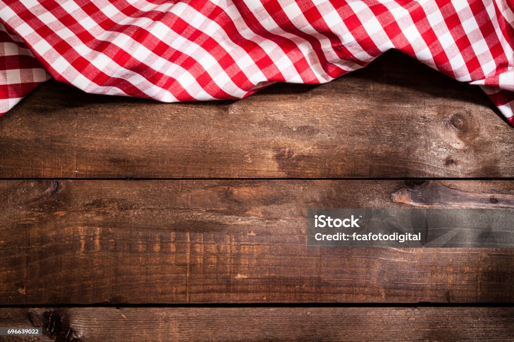 Checkered tablecloth on rustic wooden table Top view of a red and white checkered textile napkin at the top border of a rustic wooden table leaving a useful copy space for text and/or logo in the rest of an horizontal frame. Predominant colors are brown and red. Low key DSRL studio photo taken with Canon EOS 5D Mk II and Canon EF 100mm f/2.8L Macro IS USM Checked Pattern Stock Photo