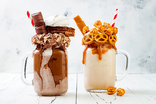 Caramel and chocolate indulgent exreme milkshakes with brezel waffles, popcorn, marshmallow, ice cream and whipped cream. Crazy freakshake food trend.