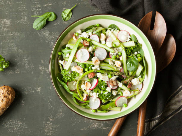 istock Spring vegetable salad with asparagus, zucchini, radish, spinach and goat cheese on dark background. 696669784