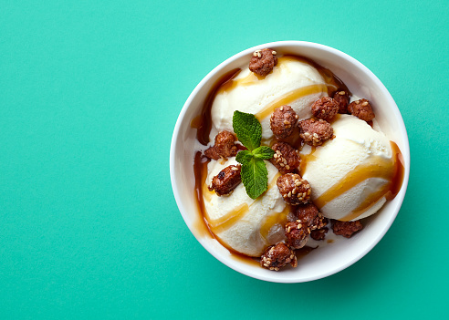 Bowl of vanilla ice cream, caramel sauce and nuts isolated on green background. Top view