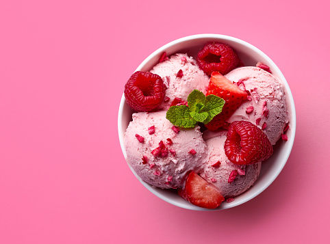 Bowl of pink strawberry ice cream and fresh berries isolated on pink background. Top view