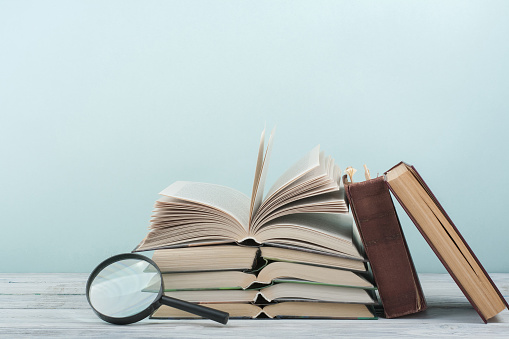 Open book, hardback colorful books on wooden table. Magnifier. Back to school. Copy space for text. Education business concept