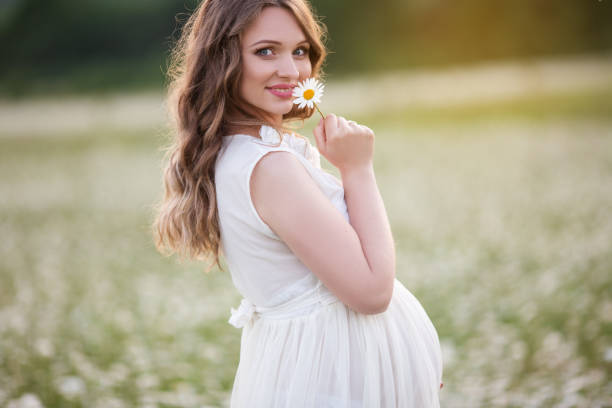 beautiful happy pregnant woman on the field of daisy flowers - dress human pregnancy young women women imagens e fotografias de stock
