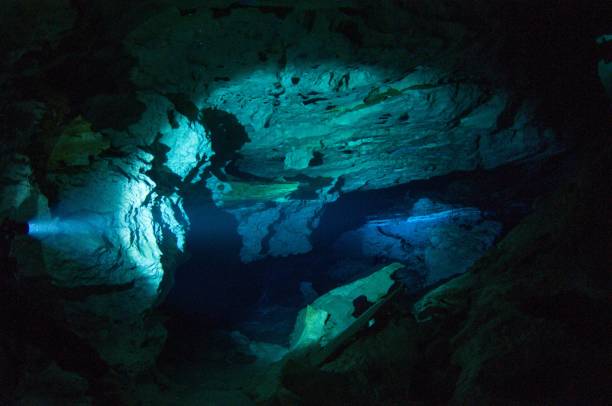 istock cavern tech sidemount diver going through small entrance in cave cenotes with flashlight viewing halocline salt and fresh water barrier 4 696693366