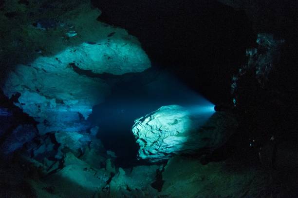 istock cavern tech sidemount diver going through small entrance in cave cenotes with flashlight viewing halocline salt and fresh water barrier 1 696693496