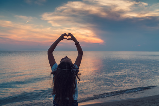 Girl at the beach showing heart shape symbol at sunset