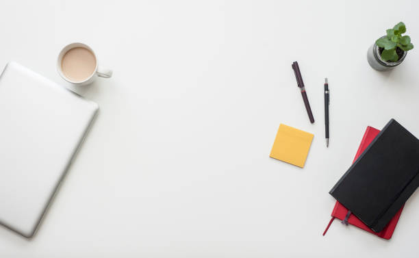 istock Trendy white office desk from the above with coffee and work related items on it: notebook, pens, Laptop 696740788