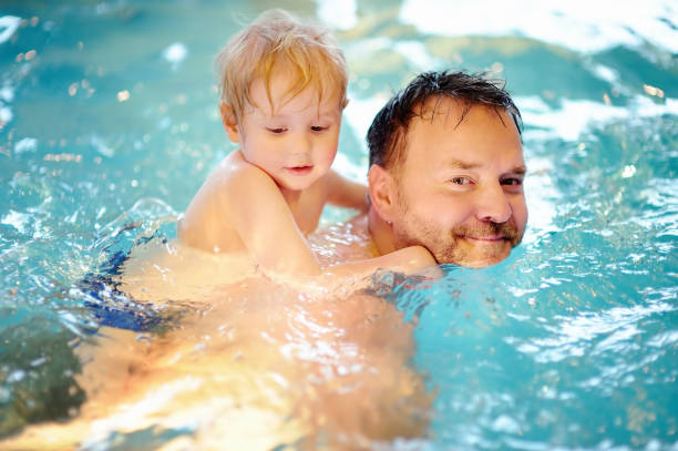 счастливый улыбающийся маленький мальчик с отцом в бассейне - swimming child swimming pool indoors стоковые фото и изображения