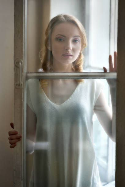 istock Beautiful woman looking through the window glass . 696752496