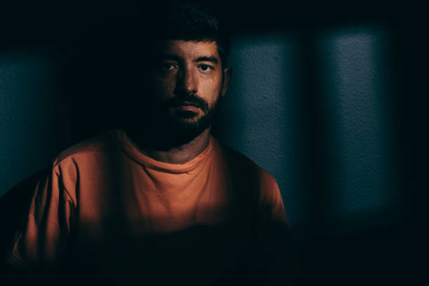 istock Prisoner man in dark cell illuminated only by a beam of light 696773638