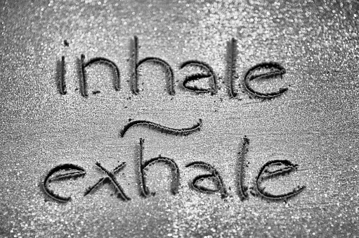 Relaxation reminder to inhale and exhale handwritten in textured sand with selective focus bokeh effect