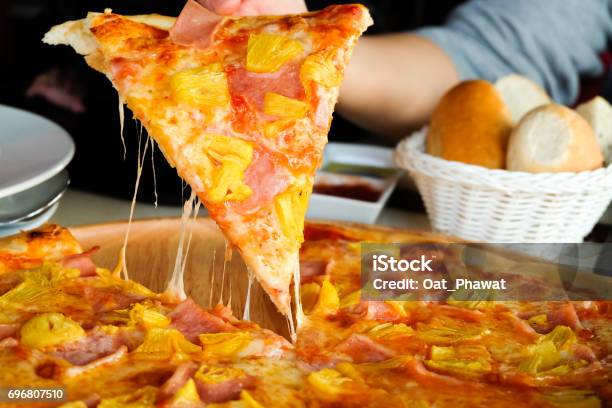 Close Up Womans Hand Picked Hawaiian Pizza From A Wooden Tray On The Table Stock Photo - Download Image Now