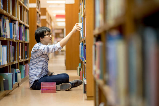 istock Young Asian man university student choosing book in library 696816710