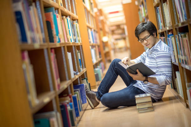 istock Young Asian man university student reading book in library 696816860