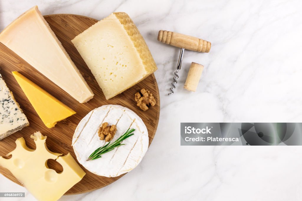 Selection of cheeses with corkscrew, cork, and copyspace An overhead photo of a selection of cheeses, shot from above on a white marble table, with a wine corkscrew and a cork, and a place for text Cheese Stock Photo