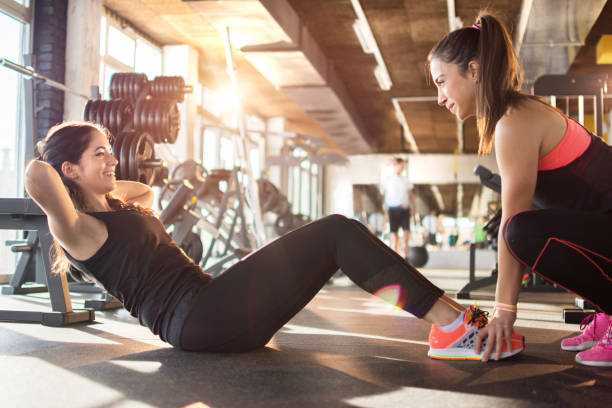 giovane donna che si allena con l'assistenza di un'amica in palestra. - fitness instructor foto e immagini stock