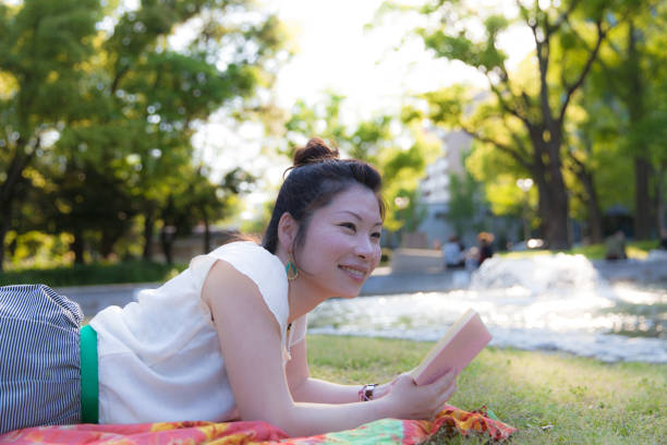 istock Japanese woman reading a book in a park 696844884