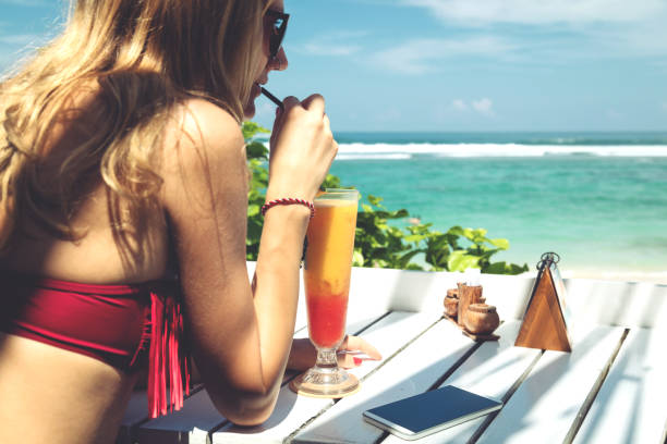 istock Young attractive girl drinking healthy juice and using a cellphone on the beach. 696847488