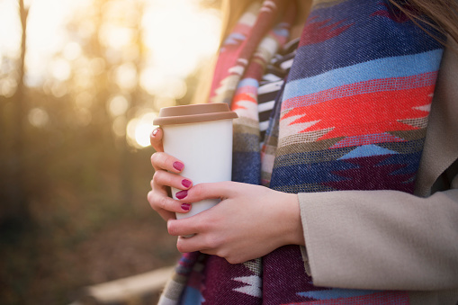 Unrecognizable woman with colorful scarf holding a coffee mug; cut out.