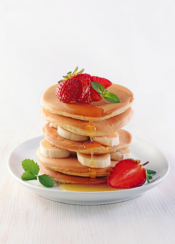 Tasty breakfast. Homemade pancakes with fresh strawberry and banana, honey and mint on white wooden background